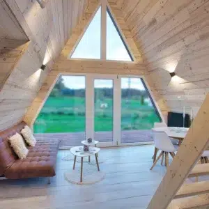 Salon vitré du chalet A-Frame Iorik – baie triangulaire, Gérardmer Salon du chalet A-Frame Iorik avec baie vitrée triangulaire pleine hauteur, canapé en cuir et vue sur la nature vosgienne, près de Gérardmer