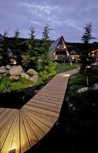 Chalet A-Frame Iorik de nuit – location près de Gérardmer, Vosges Chalet A-Frame Iorik illuminé de nuit, allée en bois menant à la terrasse, niché en forêt à 10 min de Gérardmer dans les Vosges